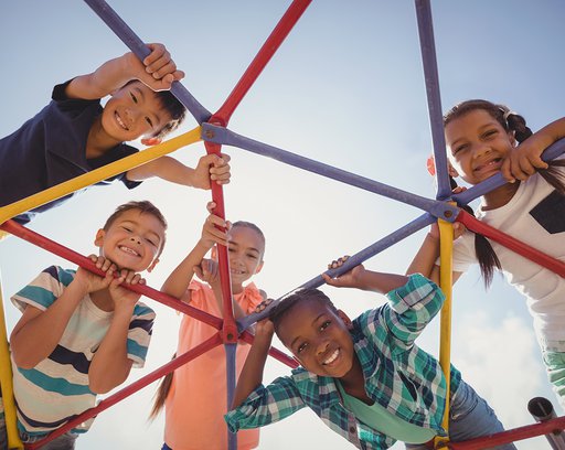 Portrait-of-happy-schoolkids-looking-through-dome-climber